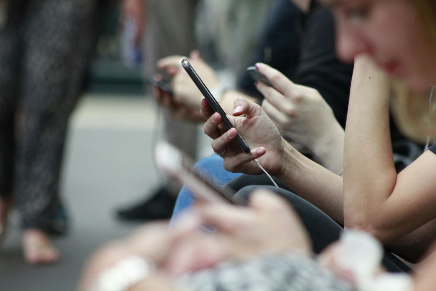 A row of people sitting side by side, each looking at their own phone